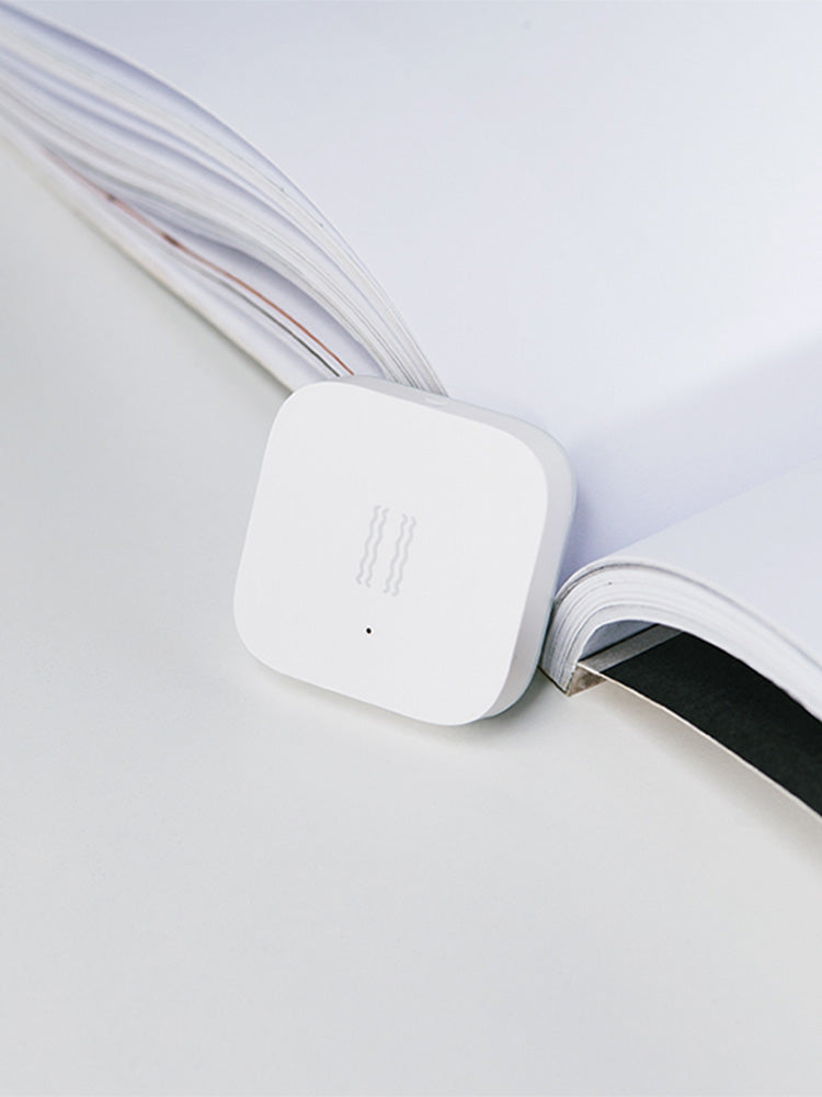 Smart Vibration Sensor Alarm placed on an opened book, showcasing its compact and sleek design.