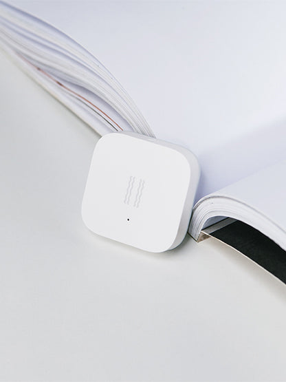 Smart Vibration Sensor Alarm placed on an opened book, showcasing its compact and sleek design.