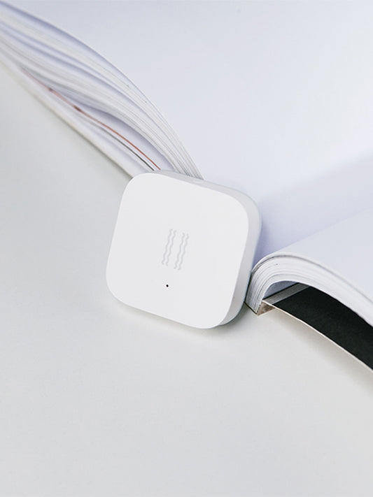 Smart Vibration Sensor Alarm placed on an opened book, showcasing its compact and sleek design.